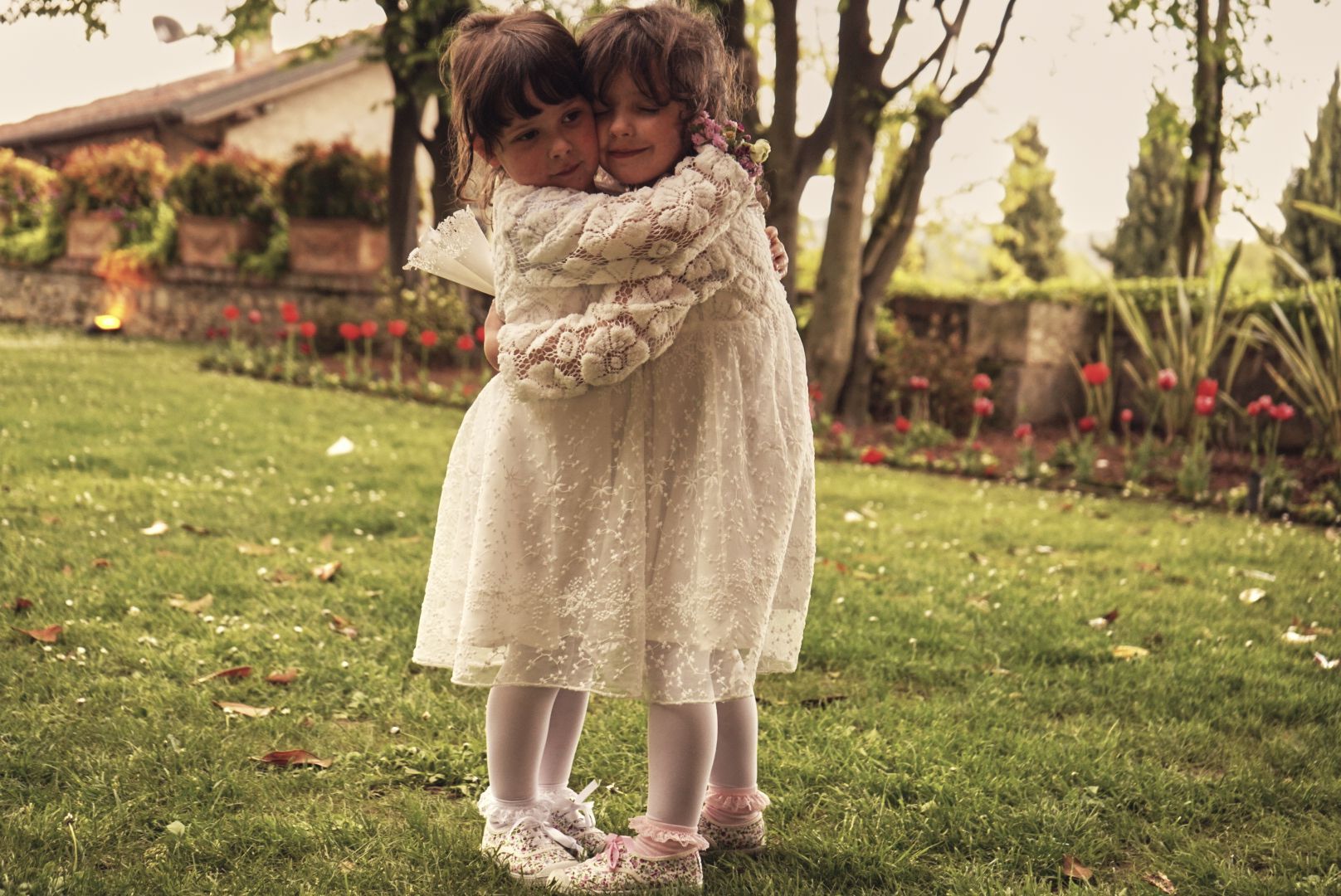 Due bambine in abito di pizzo abbracciate in giardino a un matrimonio